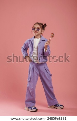 Standing and posing, holding candy. Cute little girl is against pink background.