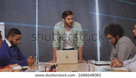 Standing project manager leaning forward at meeting table in office with laptop and data display. Collaboration, teamwork, professionalism, modernoffice, dataanalysis, businessmeeting, corporate