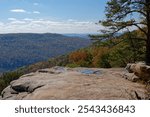 Standing at the rock edge on the cliff of Bee rock at the overlook point in middle Tennessee looking out at the mountains with trees turning colors on a bright hazy sunny day in autumn