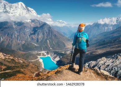 Standing woman with backpack on the mountain peak. Beautiful mountains in clouds, lake with azure water at sunset. Landscape with alone girl, snowy rocks, sky, glacier in Nepal. Travel. Trekking