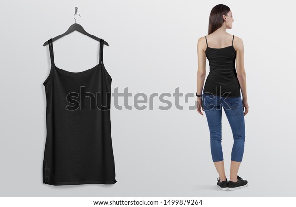 Standing woman in black\
camisole shirt in blue denim jeans pant with hanging sleeveless\
shirt on hanger 