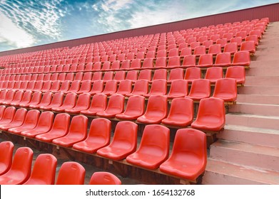 Stands for fans and spectators on an open football field. Plastic seats for spectators in a sports complex. Red benches for spectators at the stadium. Rows of plastic chairs. Gomel. The stadium 
