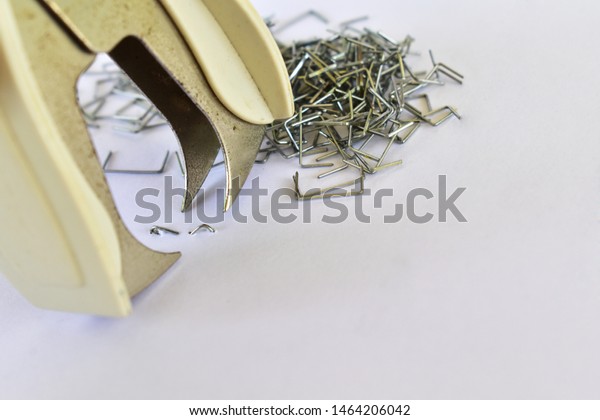 Staple pin remover with pile of staple pins \
on white background.