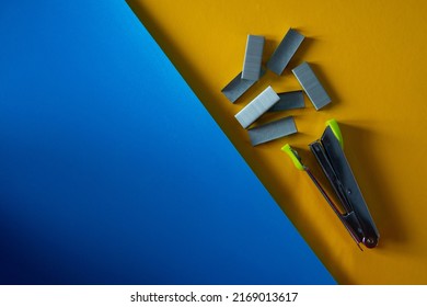 stapler and staples laying on flat blue and yellow surfaces. office tools equipment