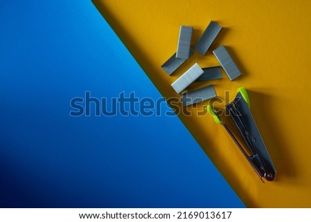 stapler and staples laying on flat blue and yellow surfaces. office tools equipment