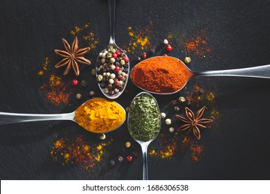 Star anis and spoons with pepper, paprika, parsley and turmeric on black background with copy space, top view. Cooking ingredients and condiments concept.