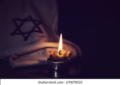 The star of David and candle stands on the table on a black background in memory of the victims of the Holocaust and genocide.
