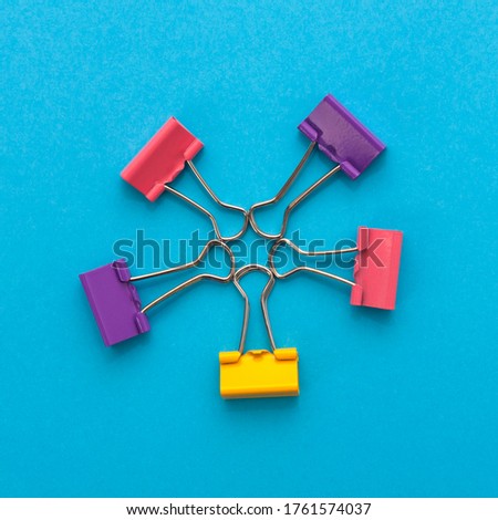 Star shape made of five colored binder clips on blue paper background, top view