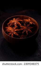 Star shaped spice star anise in a wooden round bowl on a dark concrete background