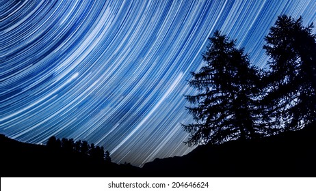 Star Trail Effect Over Mountain And Trees In Night Sky 