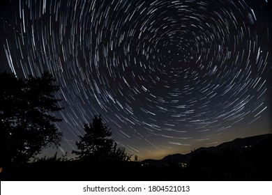 Star trail photograph around the North Polar star with hills, trees and house lights. - Powered by Shutterstock