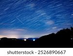 Star trails of a Milky Way with meteor, shooting stars and countryside silhouettes.