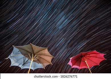 Star trails over white and red umbrellas. time lapse exposure starry nightlight. star rain. star fall.