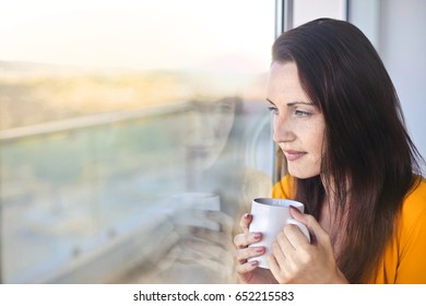Staring out of the window while drinking from a cup