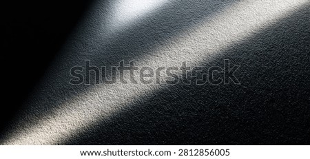 A stark diagonal beam of light cuts across a dark, textured surface, creating a strong contrast between light and shadow.