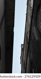 A stark perspective looking up at the sky framed by tall, worn building exteriors. Urban claustrophobia or hopeful light.