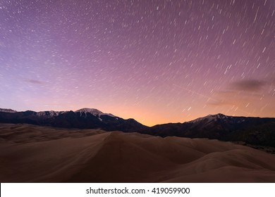 Starry Night At Great Sand Dunes - Star Trails Of Spring Night Sky Above Snow Peaks And Sand Dunes At Great Sand Dunes National Park & Preserve, Colorado, USA.