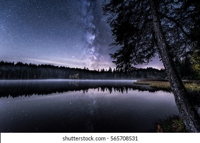 a starry night sky at a lakeside with visible milky way clearly reflected in the water 