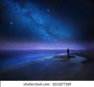 Starry night sky over sea and beach with man silhouette. man standing on sea beach under starry sky.