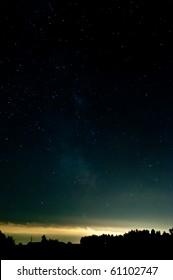 Starry Sky. Clouds At The Horizon Lighting From The Lights From A City. Contours Are Visible From A Wood.