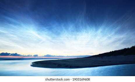 Starry sky with noctilucent clouds above the Baltic sea shore at summer solstice night. Golden flowing sunlight. Long exposure. Fantastic cloudscape. Natural pattern. Abstract art. Latvia