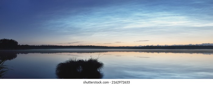 Starry sky with noctilucent clouds and fog above the Saimaa lake at summer solstice night. Golden sunlight. Long exposure. Epic cloudscape. Natural pattern. Symmetry reflections on the water. Finland - Shutterstock ID 2162972633