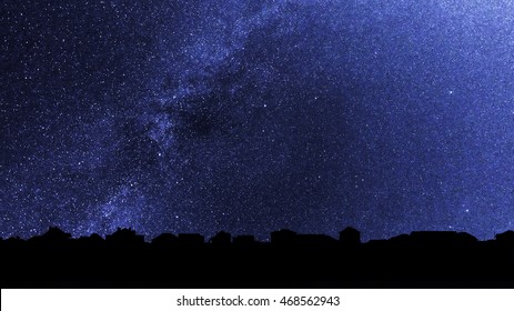 Starry sky over the roofs of suburban houses. Background with millions of stars over the village. Dark skyline in the backlighting. - Shutterstock ID 468562943
