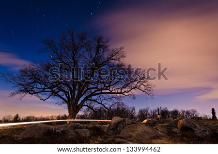 Stars and clouds move through the sky behind a tree at night near Devil's Den, Gettysburg, PA