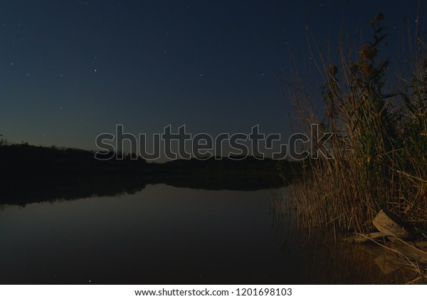 the stars in the night sky are reflected in the\
mirror smooth surface of the lake, and the moon illuminates the\
forest on the opposite bank