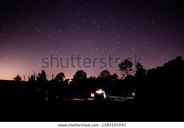 Stars and space dust in the\
universe, over a car on the road. Long exposure\
photograph.