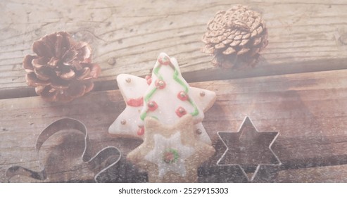 A star-shaped cookie with green and red icing sits between pine cones. Wooden surface holds cookie cutters and dusting of flour, suggesting baking - Powered by Shutterstock