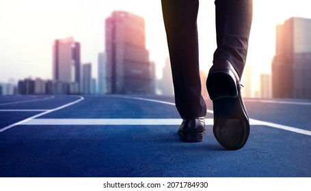 Start, Competition Concept. Low Section of Businessman Steps into Start Line on Running Track and Moving Forward to New Challenge. Blurred City Building as background - Shutterstock ID 2071784930