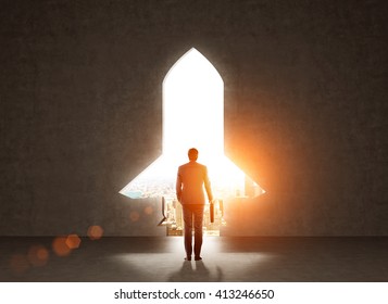 Start up concept with businessman holding briefcase and standing in front of rocket shaped gap in wall, revealing sunlit New York city view