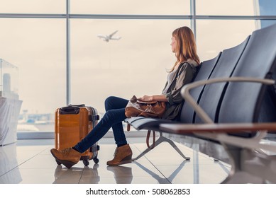 Start of her journey. Beautiful young woman looking out window at flying airplane while waiting boarding on aircraft in airport lounge