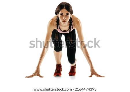 At start line. Front camera view of young female runner getting ready to run isolated on white studio background. Sport, track-and-field athletics, competition concept. Copy space for ad, text
