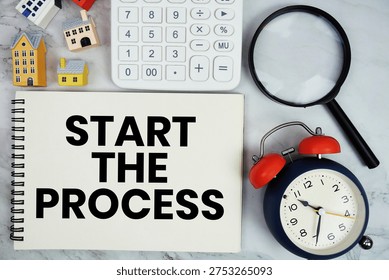 Start The Process text written on notepad with house model, calculator, magnifying glass and alarm clock on marble background