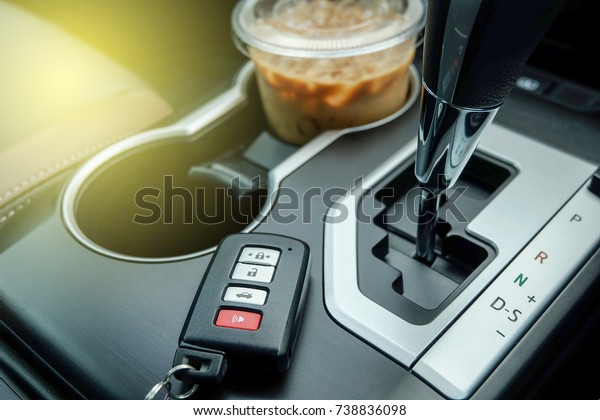 Start a Road trip with coffee, Remote car push on\
console near transmission gear vehicle and ice espresso coffee in a\
cup holder.