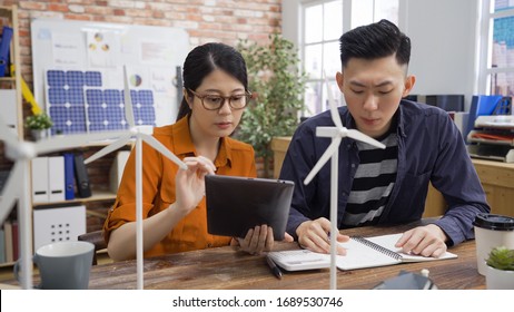 Start Up Small Business Team In Eco Friendly Office Working Showing Tablet. Talented Engineers Consider Wonderful Model Of Powerful Windmill Generators. Asian Girl And Boy Colleagues Brainstorming.