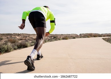 Start Of Young Black Runner In A Yellow Rain Jacket Who Enjoys Listening To Music On His Cell Phone While Training.