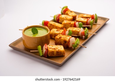 Starter snack Paneer Tikka with stick in plate with green chutney isolated over white background. Indian cuisine dish with grilled cottage cheese with vegetables and spices