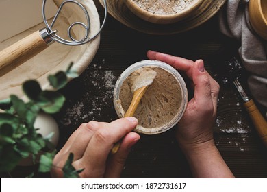 Starter sourdough. Female hands holding a jar with sourdough over wooden background.