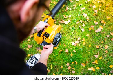 Starting A Handheld, Cordless, Electric Leaf Blower In A Garden, Selective Focus. Autumn, Fall Gardening Works In A Backyard, On A Lawn, Grass. Garden Works. 