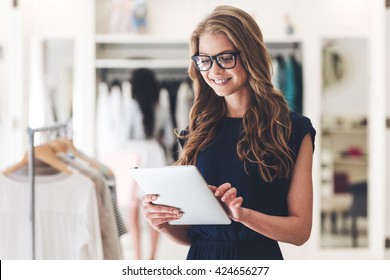 Starting new business. Beautiful young woman using digital tablet with smile while standing at the clothing store 