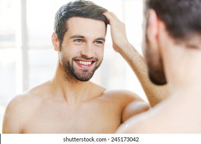 Starting New Day With Smile. Handsome Young Man Touching His Hair With Hand And Smiling While Standing In Front Of The Mirror