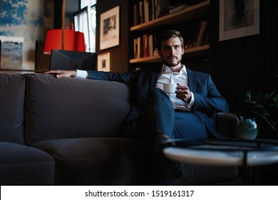 Starting new working day. Handsome young man holding coffee cup sitting on the couch in office