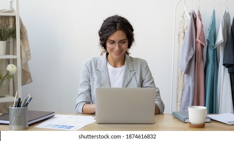 Starting workday. Happy young businesswoman self-employed tailor receive customers orders by email. Smiling lady fashion designer sitting at desk. Receptionist in atelier sewing workshop using laptop - Powered by Shutterstock