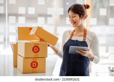 Startup happy Asian woman business owner works with a box at home, prepare parcel delivery SME supply chain, procurement, package box to deliver to customers, Online SME business entrepreneurs ideas,