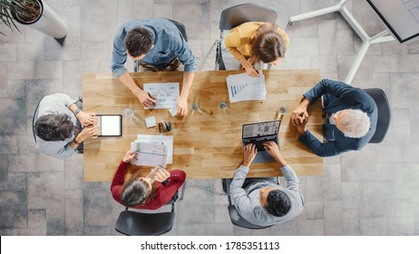 Startup Meeting Room: Team of Entrepreneurs sitting at the Conference Table Have Discussions, Solve Problems, Use Digital Tablet, Laptop, Share Documents with Statistics, Charts. Top View