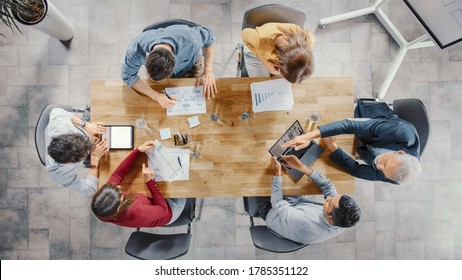 Startup Meeting Room: Team Of Entrepreneurs Sitting At The Conference Table Have Discussions, Solve Problems, Use Digital Tablet, Laptop, Share Documents With Statistics, Charts. Top View