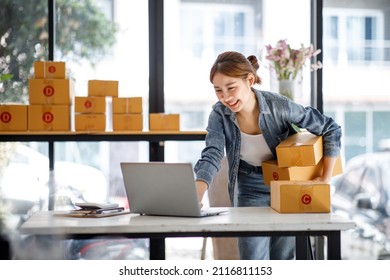 Startup Small Business Entrepreneur Or Freelance Asian Woman Using A Laptop With Box, Young Success Asian Woman With Her Hand Lift Up, Online Marketing Packaging Box And Delivery, SME Concept.